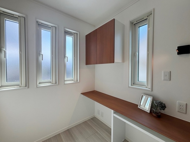 2階の書斎で、木製のデスクと棚が設置されています。壁には収納棚があり、小さな装飾品や写真立てがデスクに置かれています。在宅ワークや勉強、趣味に適した落ち着いた空間です。