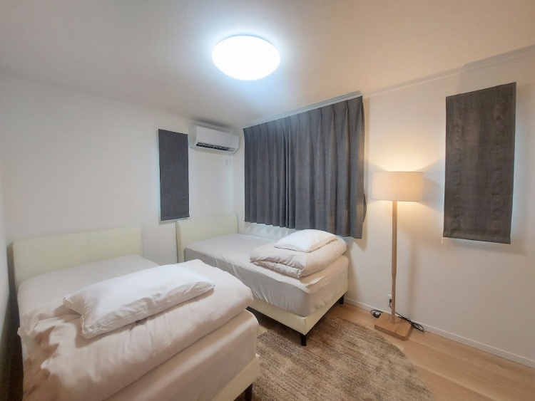 シンプルで落ち着いた雰囲気のベッドルーム。白を基調とした壁と明るいフローリングに、2台のベッドが並べられています。