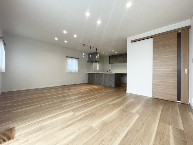 グレーの石目調キッチンカウンターと、温かみのある木目調の引き戸が調和した、広々として明るいLDKです。