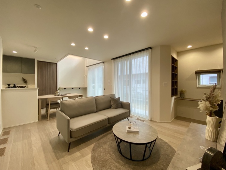 落ち着いた雰囲気のリビングダイニング。グレーのソファとラウンドテーブルが上品な空間を演出し、大きな窓からは柔らかな自然光が差し込みます。