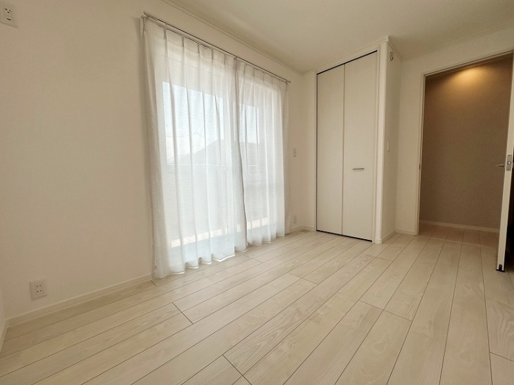 広々とした部屋に、大きな窓と柔らかい白いカーテンがあり、外の光が室内に柔らかく入っています。床は明るい木目調で、全体的に明るく開放感のある空間です。