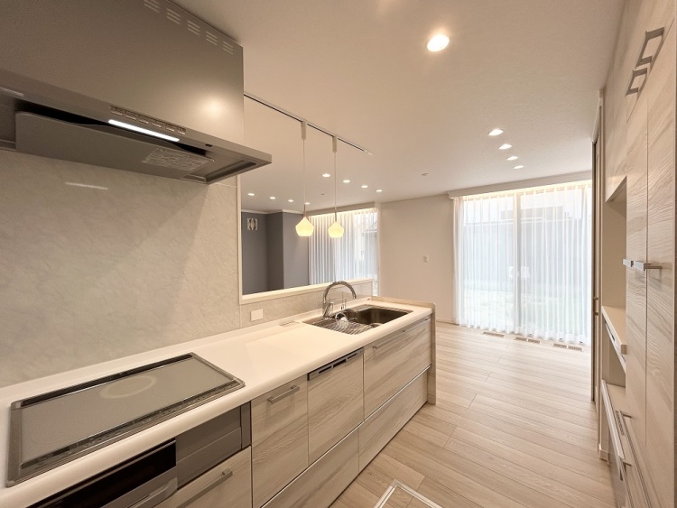 大きな窓から自然光がたっぷりと差し込むキッチンで、白を基調とした内装がやさしく光を反射し、清潔感のある空間が広がっています。