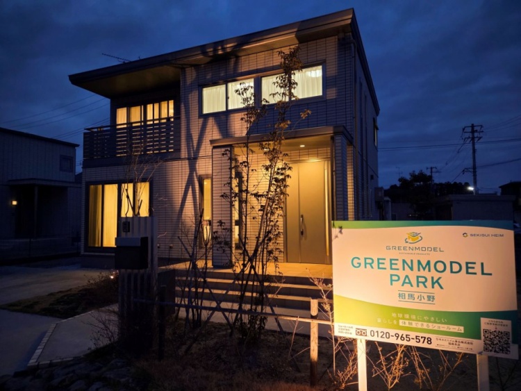 青空の下に建つ二階建ての住宅で、広い窓と整った庭が明るく開放的な印象を与えています。周囲には静かな住宅街が広がっています。