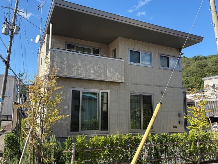 薄黄色の外壁の２階建て住宅のB棟外観。玄関には小さな階段があり、植栽が植えられています。庭も見えます。