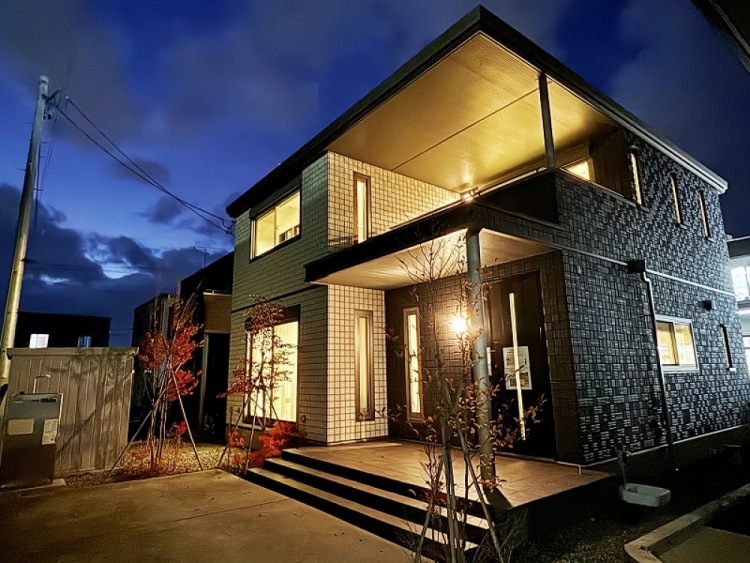 黒と白い外壁の二階建て住宅の外観。家の前には小さな木々が植えられており、バルコニーと玄関の屋根が特徴的です。清潔感があり、シンプルで洗練された外観です。