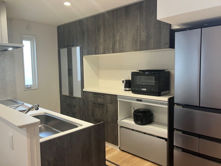 落ち着いた色合いの木目の収納に囲まれたキッチン。電子レンジや炊飯器が並び、整った印象の作業スペースが広がっています。