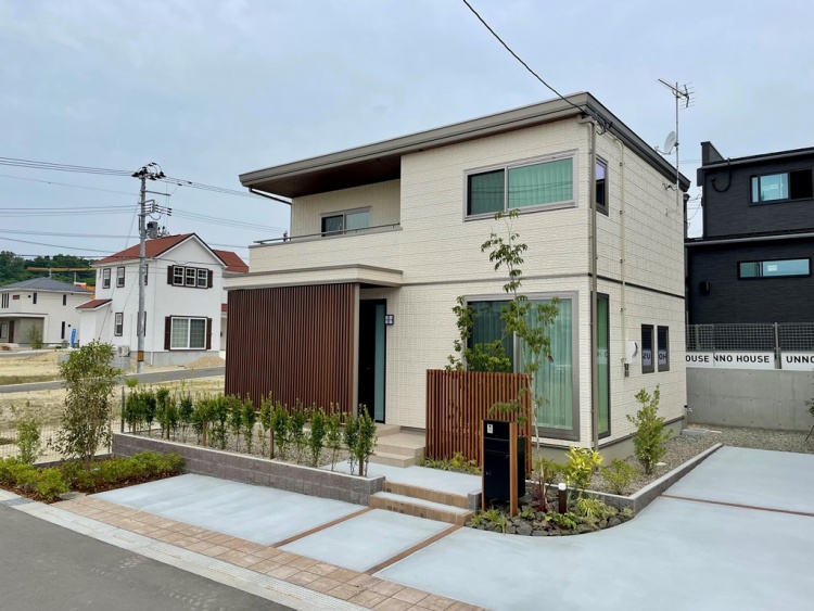 ベージュの外壁の二階建て住宅のA棟外観。庭には植栽が植えられ、駐車スペースも備わっています。