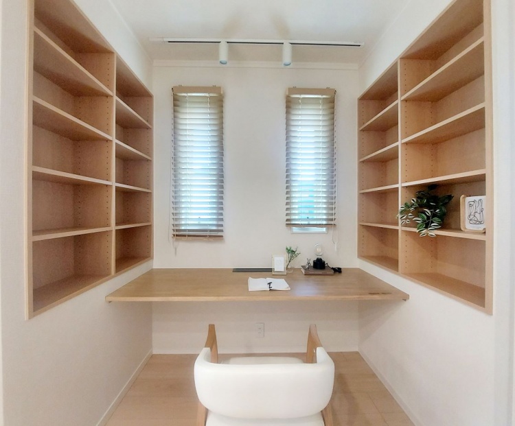 両側に本棚が並ぶ小部屋に、窓からの光がやさしく差し込み、机の上に穏やかな雰囲気が広がっています。