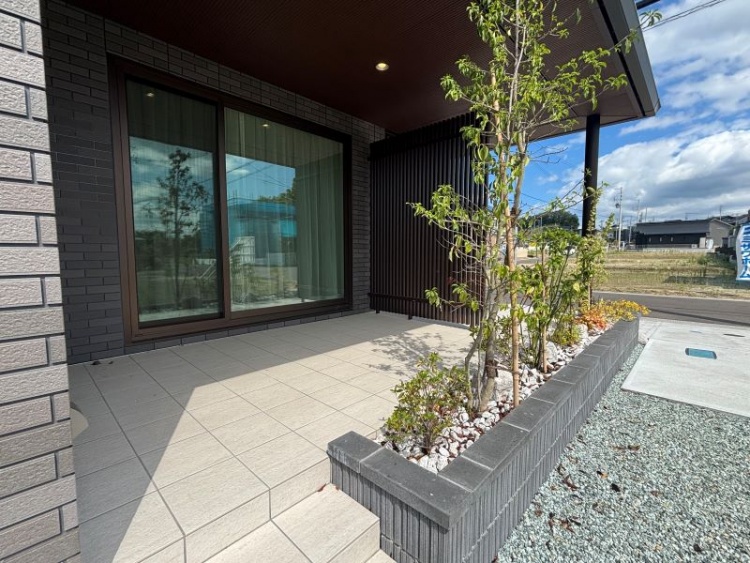 玄関ポーチ横に広がるタイル敷きのテラススペース。縦格子と植栽が目隠しの役割を果たし、外からの視線を程よく遮りながら、屋外でも落ち着いた時間を過ごせる空間を演出しています。