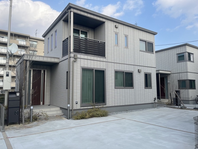 白い外壁の2階建て住宅の外観。玄関の左前には黒いポストがあり、植栽が植えられています。手前には駐車場が見えます。