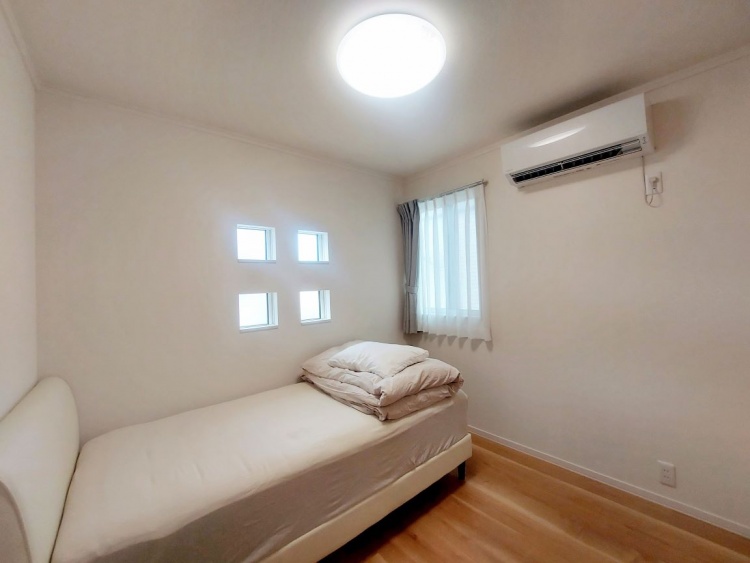 明るくコンパクトなベッドルーム。白を基調とした内装に、シングルベッドが1台設置されています。壁には小さな正方形の窓が6つ並んでおり、デザイン性と採光性を兼ね備えています。