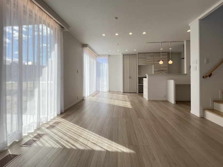 大きな窓から柔らかな光がレースのカーテン越しに差し込むリビングで、木の床があたたかみを添え、心地よい空間が広がっています。