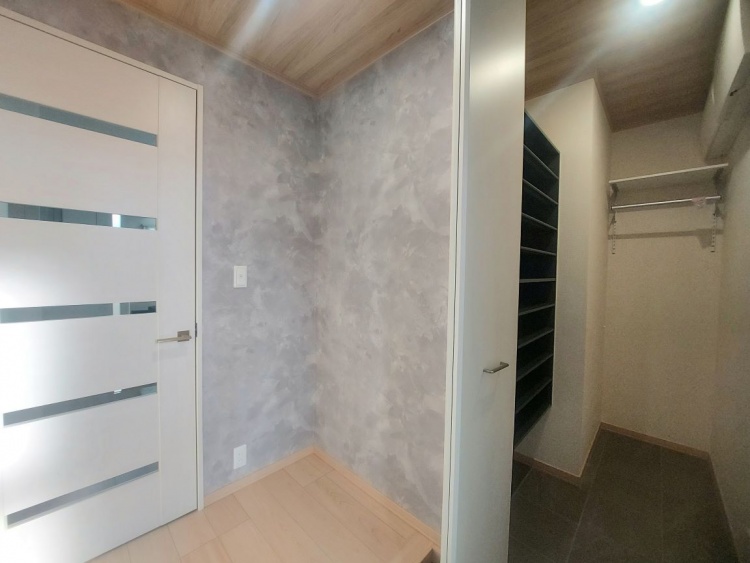 木目の天井と深い色の棚が落ち着いた雰囲気を醸し出す玄関で、靴や荷物をすっきりと収められる空間です。