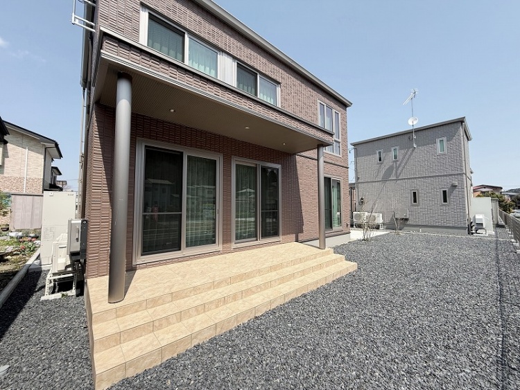 屋根付きのテラスがあり、3段の階段が設置された建物の外観。ベランダから部屋の中に入れる窓が見えます。