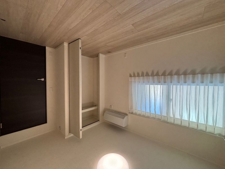 白を基調とした寝室。エアコン、収納、L字型の窓が設置されています。