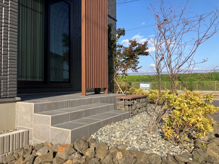 縦長の窓と格子が特徴的な黒い外壁の家の玄関で、植栽と石が美しく配置され、静けさと品のある佇まいです。