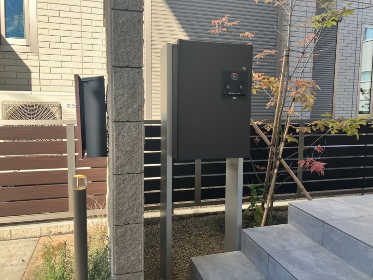 住宅の玄関先に設置されたスマートな宅配ボックス。スタイリッシュなブラックカラーで、モダンな外観に調和しています。