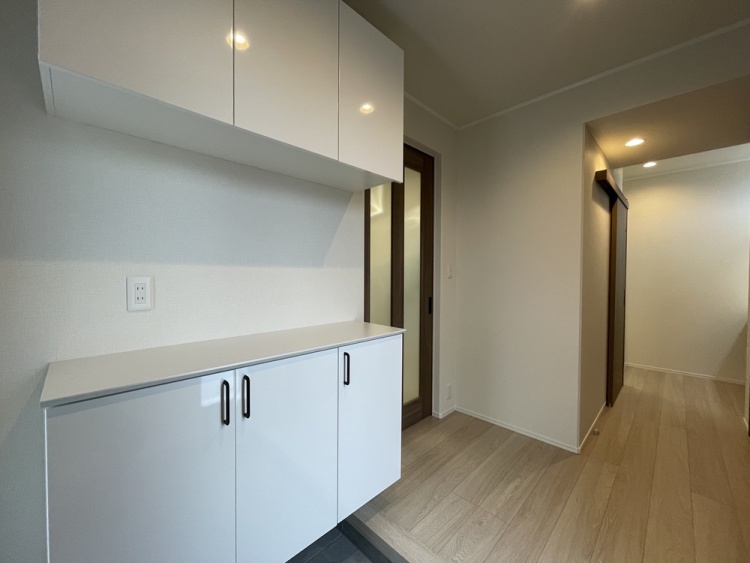 白い扉付き収納のある玄関スペースから、奥へと伸びる廊下が見えます。必要な物をすっきり収めながら、家の中へ自然に気持ちを切り替えられる場所です。