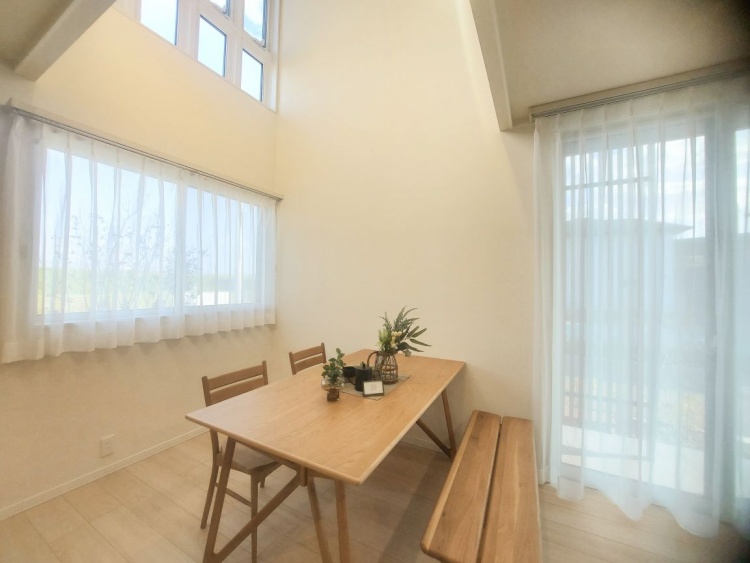 高い窓と大きなカーテンから柔らかな光が差し込み、木のテーブルとベンチが温もりを感じさせています。