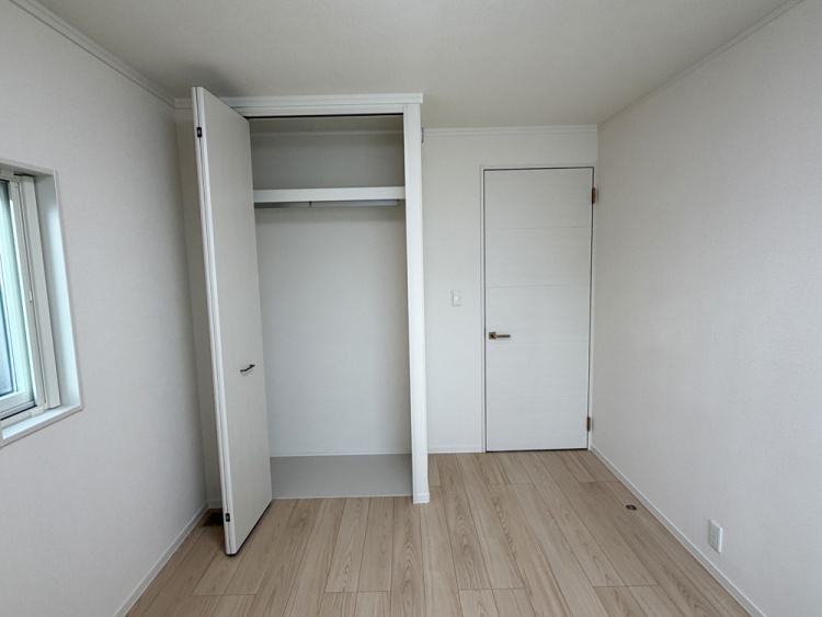 白を基調とした寝室。収納スペースと、右側に開いたドアが見えます。