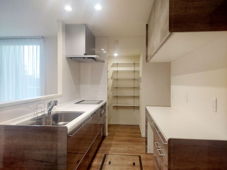 木目調の収納と白いカウンターが並ぶ広々としたキッチンで、奥には便利なパントリーがあります。