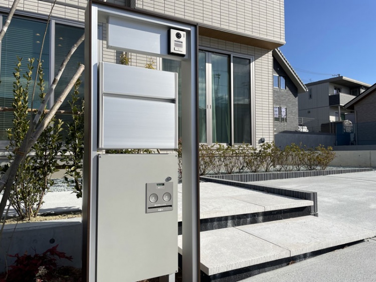 住宅の玄関前にある宅配ボックスとインターホン。背景には庭が見えます。