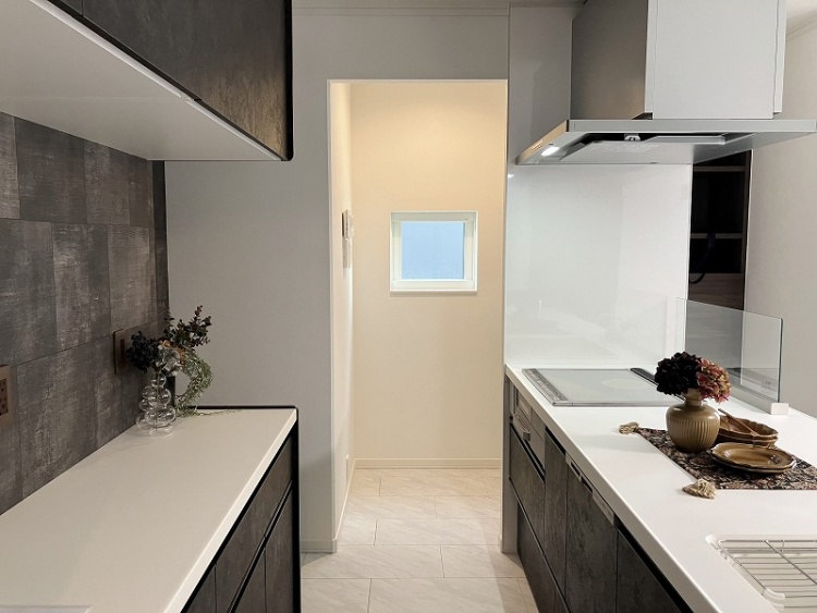モノトーンの配色が美しいキッチン。黒い収納と白いカウンターが調和し、洗練された印象。広い調理スペースが確保され、作業しやすい設計。奥には収納棚が備えられ、キッチン家電や調理道具をすっきりと収納できる。
