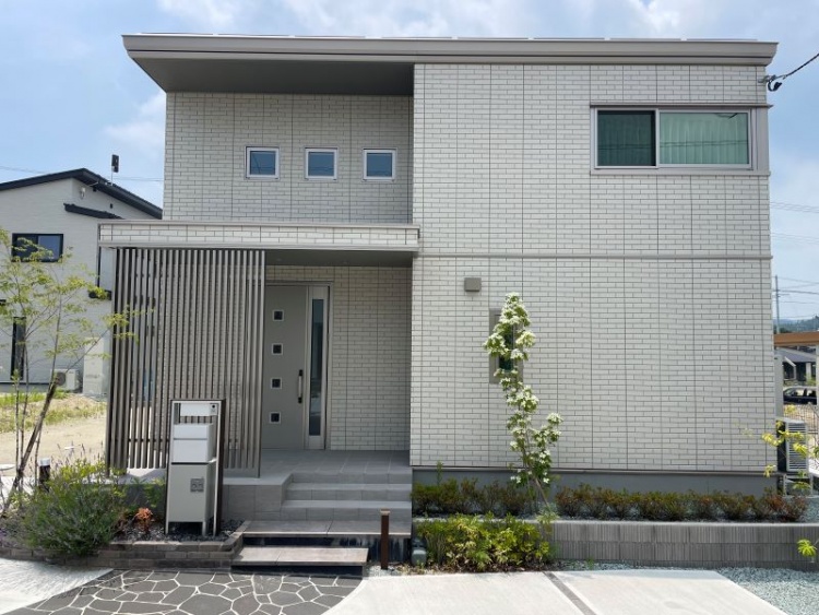 白いタイル壁の２階建て住宅E棟の外観。庭とエントランスが見えます。