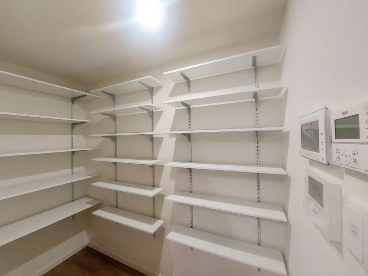 明るい照明に照らされた広々としたパントリーで、暮らしを便利にするたっぷりの収納が広がっています。