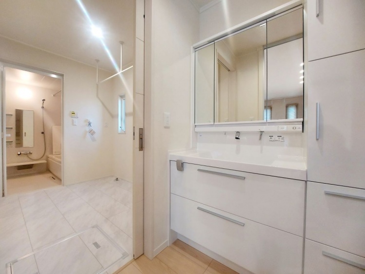 白を基調とした洗面所に大きな鏡があり、奥には明かりに照らされた浴室が見えています。