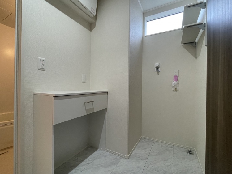 明るい床材の洗面脱衣室にあるランドリースペースです。窓付きで換気しやすく、壁面には収納棚が設置されています。