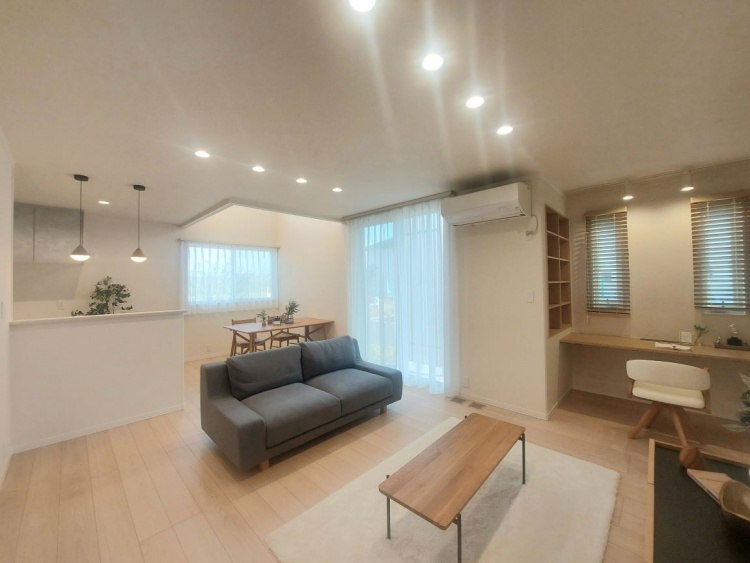 やわらかな光が広がるリビングダイニング。グレーのソファと木の家具が温かみを添え、奥には作業ができるカウンタースペースもあります。