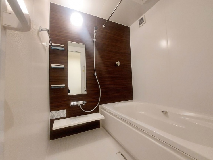 白い浴槽と木目調の壁が調和した浴室で、鏡とシャワーがすっきりと配置されています。