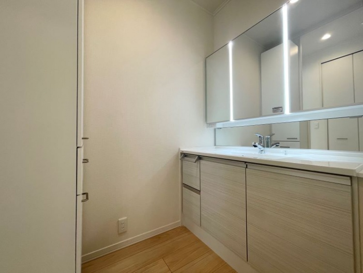 大型ミラーと明るい照明が特徴の洗面化粧台。収納力のある引き出し式キャビネットと清潔感のあるナチュラルな色合いで、使い勝手とデザイン性を兼ね備えた空間です。