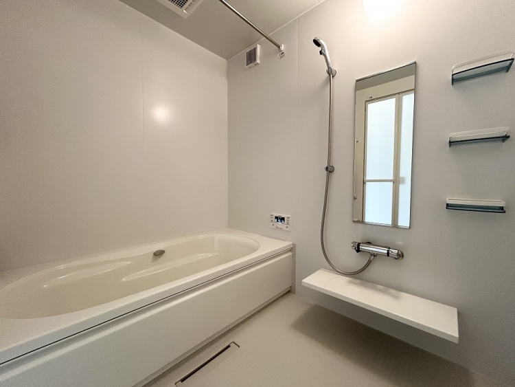 壁も床も白で統一された浴室で、明るく清潔な印象を与えます。浴槽やシャワー、棚がすっきりと配置されています。