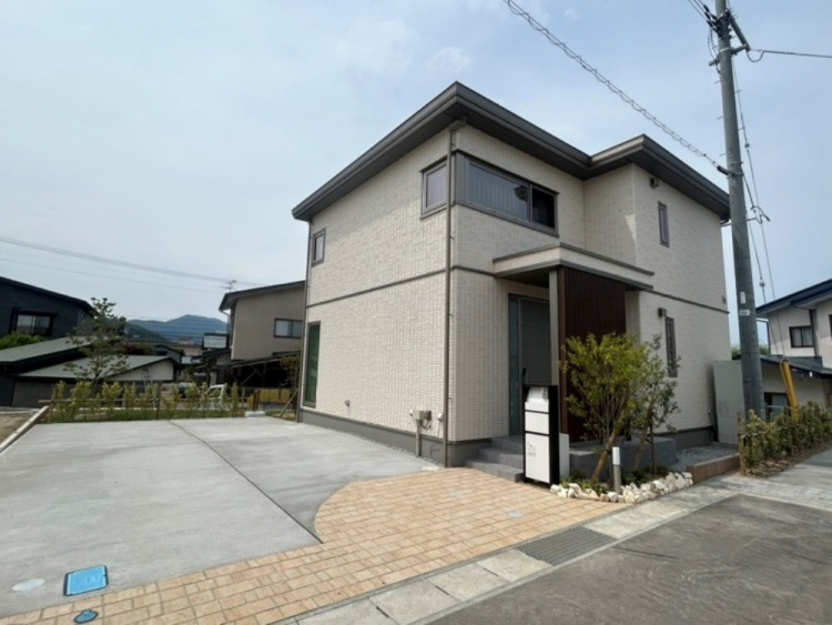 白い壁の二階建て住宅。玄関ドアの前に格子があり、プライバシーが保たれている。