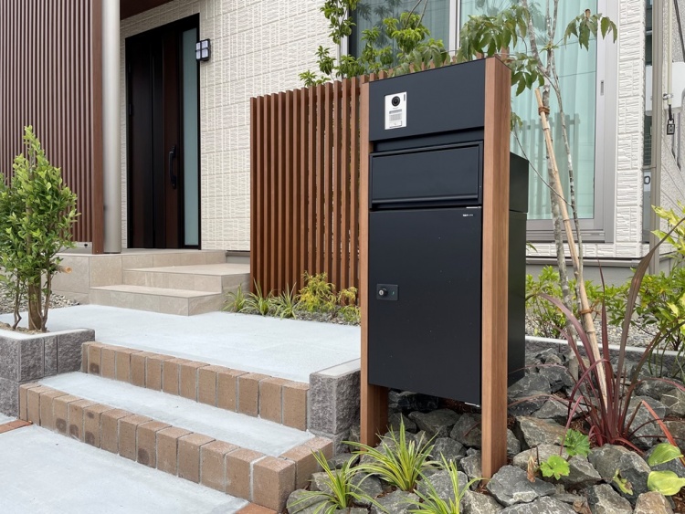 Ａ棟の玄関。黒い宅配ボックスが設置され、階段と植栽が植えられています。