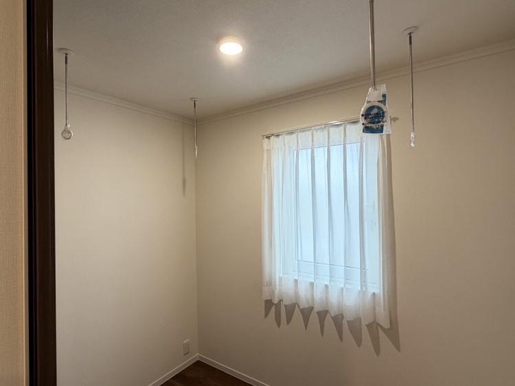 小さな窓に白いカーテンがかかった、明るいサンルームです。天井には照明器具が取り付けられており、左側にはエアコンが設置されています。