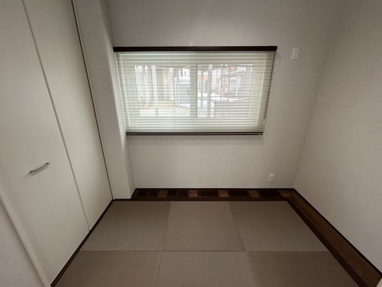シンプルで落ち着いた和室の一角。畳敷きの床が心地よい雰囲気を演出し、窓にはブラインドがかかっている。左側には白いクローゼットがあり、収納にも便利な空間。