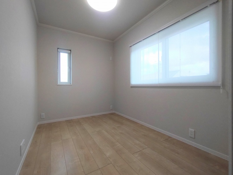 シンプルでコンパクトな洋室。ナチュラルな木目のフローリングと白い壁が清潔感を演出しています。大きな窓からは自然光がたっぷり入り、室内を明るくしています。細長い縦窓もアクセントになっており、空間に軽やかさを与えています。