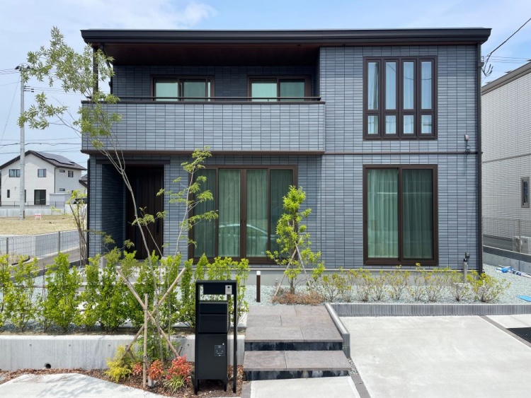 ネイビー色の外壁の二階建ての住宅のA棟外観。手前には庭、植栽が植えられていて、黒いポストが設置されています。