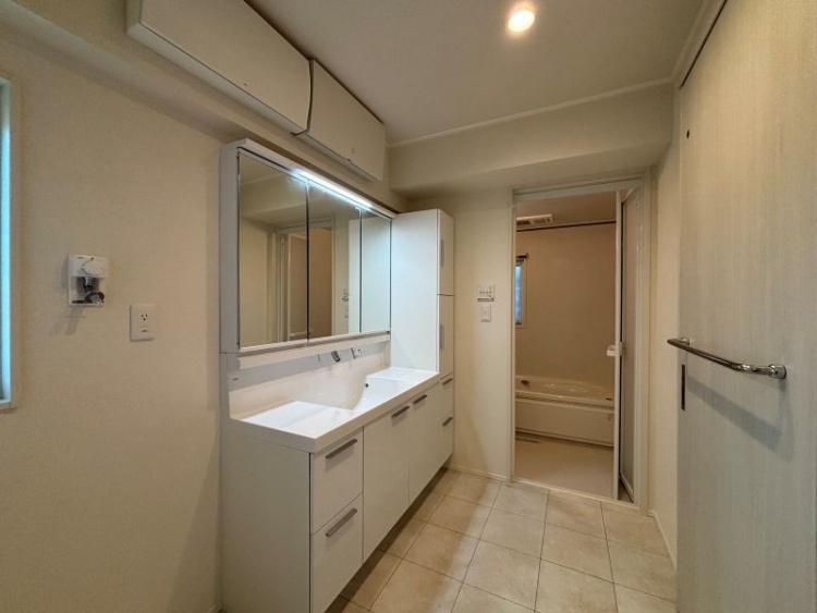 白を基調とした3面鏡の洗面脱衣室。収納や棚、小窓もあります。奥に浴室が見えます。