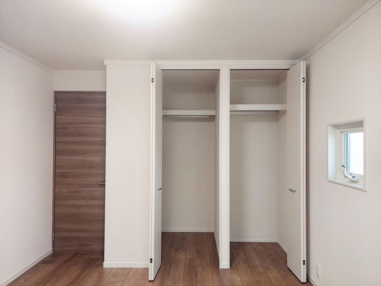白い折れ戸のクローゼットが開かれた部屋で、木目の床と白い壁が落ち着いた雰囲気を作っています。