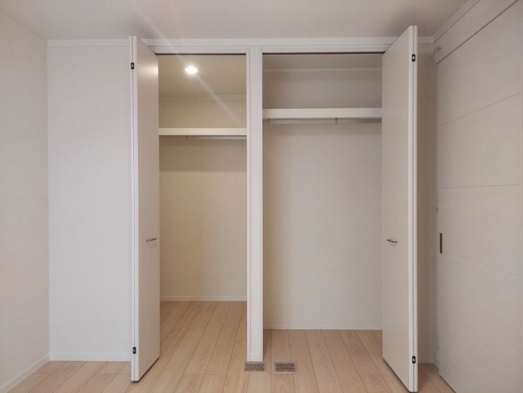 白い扉が左右に開かれたクローゼット。中には洋服を掛けるポールがあり、床はやさしい木目のフローリングです。