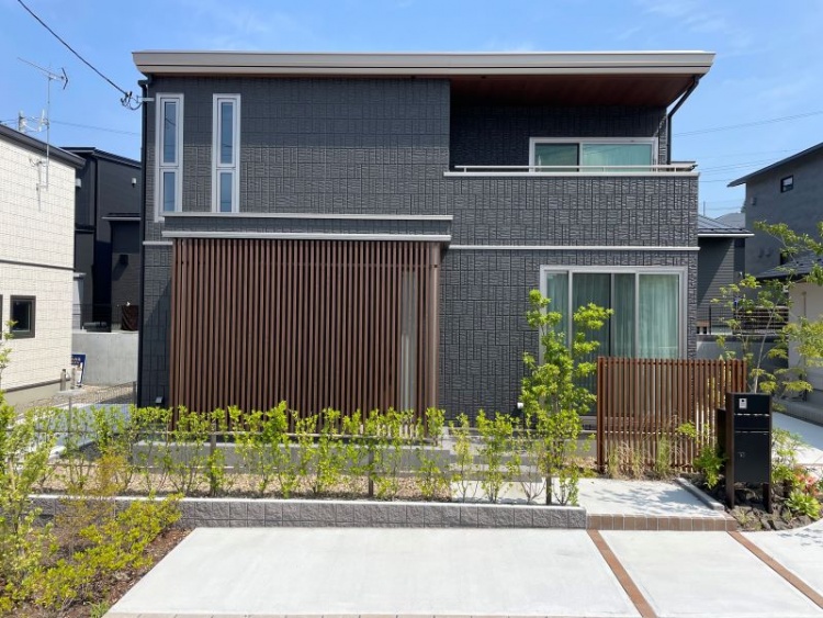 ダークグレーの外壁と木目調ルーバーを基調とした２階建て住宅のB棟外観。前庭には植栽が植えられています。
