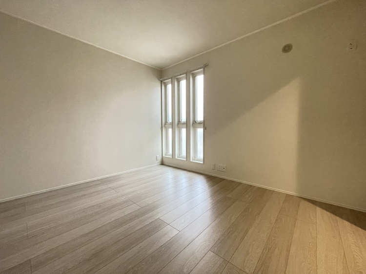 縦長の窓から自然光が入るシンプルな洋室です。明るいフローリングと白を基調とした内装が特徴です。