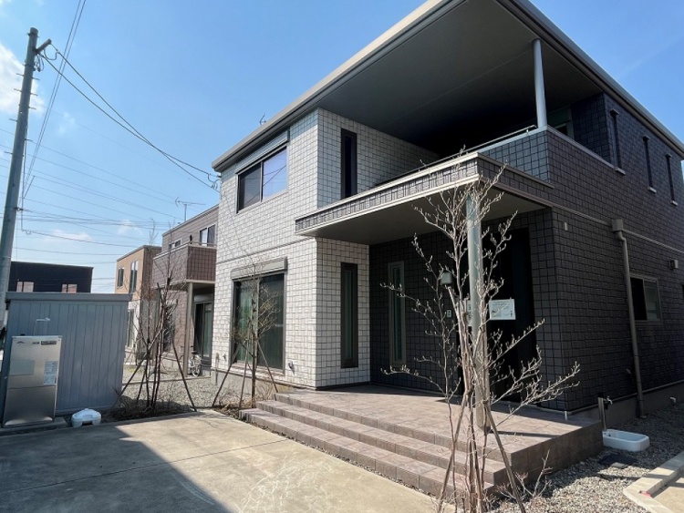 黒と白い外壁の二階建て住宅の外観。家の前には小さな木々が植えられており、バルコニーと玄関の屋根が特徴的です。清潔感があり、シンプルで洗練された外観です。