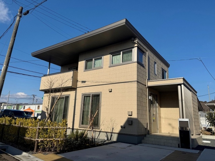 薄黄色の外壁の２階建て住宅のB棟外観。玄関には小さな階段があり、植栽が植えられています。庭も見えます。
