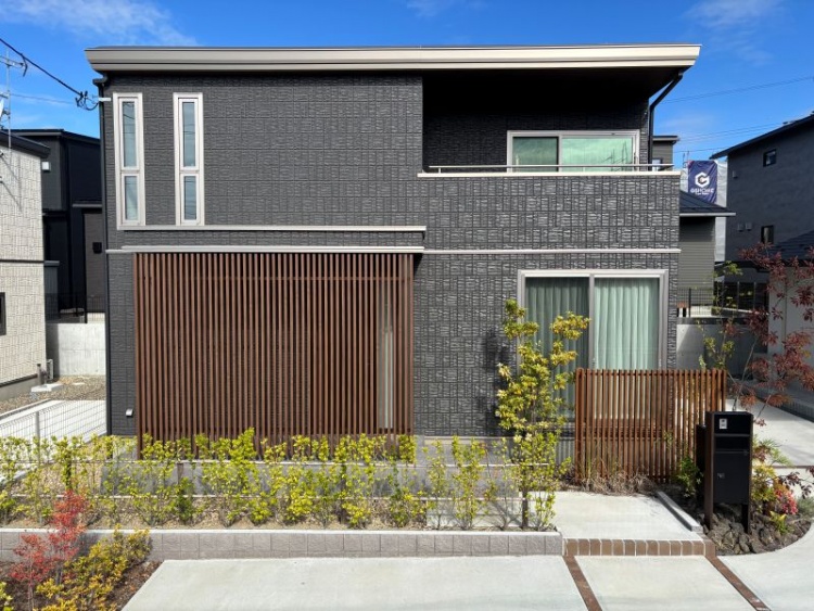 ダークグレーの外壁と木目調ルーバーを基調とした２階建て住宅のB棟外観。前庭には植栽が植えられています。