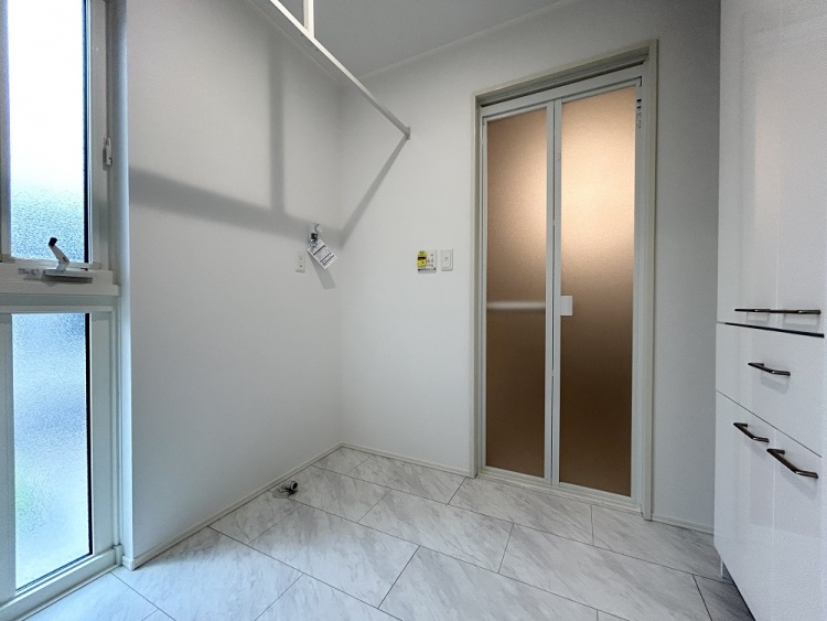 洗濯機の設置を想定したスペースに、物干し用のバーと収納が備わっており、洗濯や家事がしやすいように整えられた空間です。